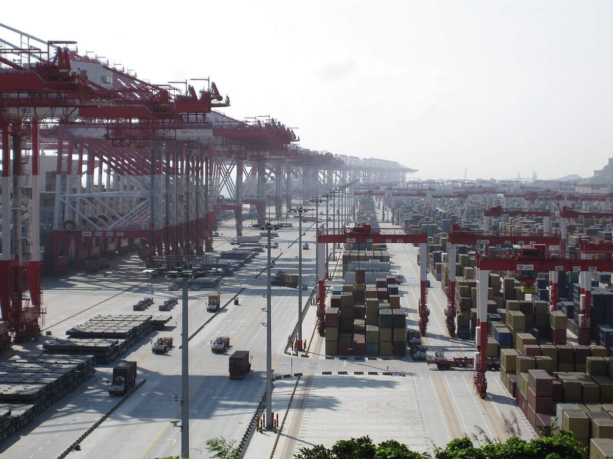 Aerial view of a Chinese container port at dusk with stacked boxes waiting for vessels, representing the backlog building at Yangshan and Ningbo as chemical factory output drops through December 2022